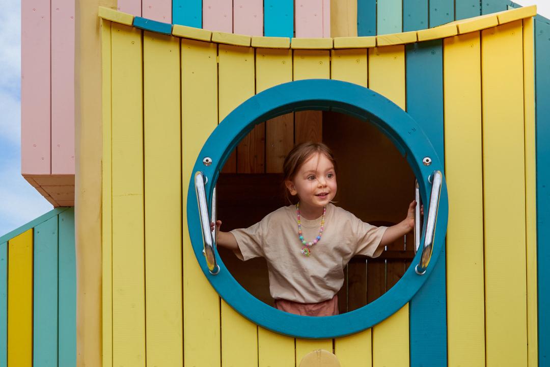 Girl peeking out from giant birdhouse at playground
